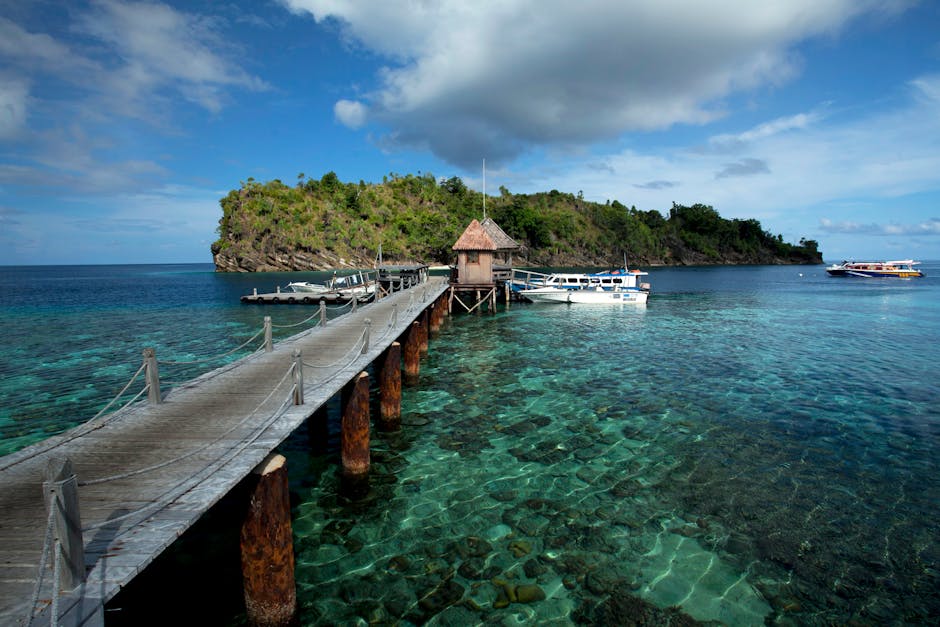 A wooden pier leads out over crystal clear water to a tropical island