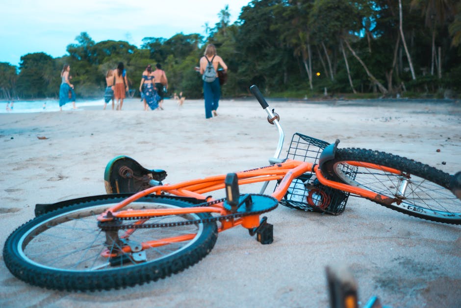 A lively orange bicycle lying on a sandy beach