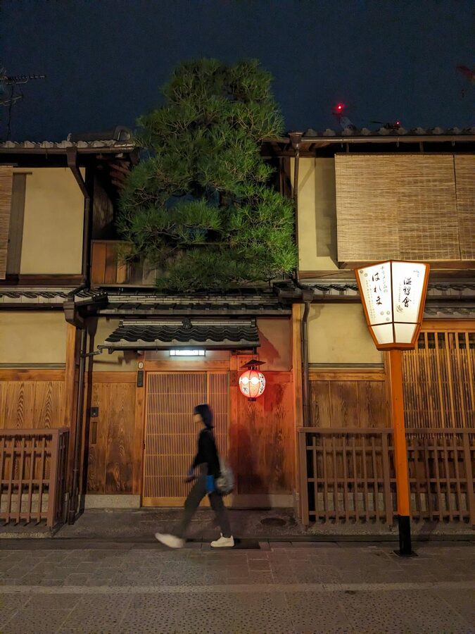 Person walking past traditional wooden buildings in Kyoto Gion district at night