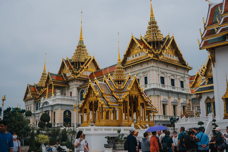 Tourists walking through the Grand Palace complex with golden temple buildings in Bangkok
