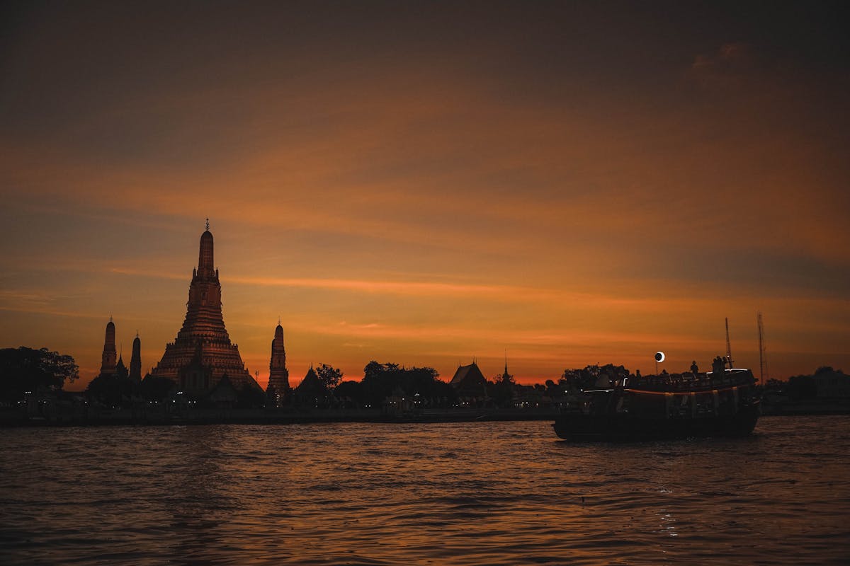 Silhouette of Wat Arun temple against a colorful sunset sky along the Chao Phraya River in Bangkok