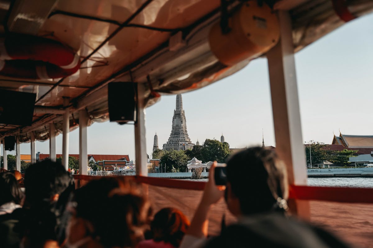 People on a boat taking photos of Wat Arun temple from the Chao Phraya River in Bangkok