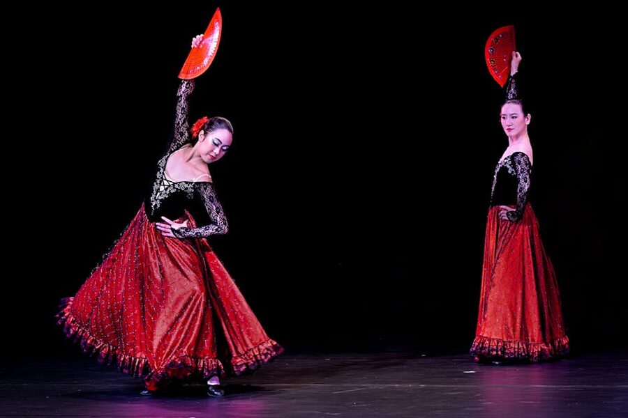 Flamenco dancers performing with red fans on a tablao stage