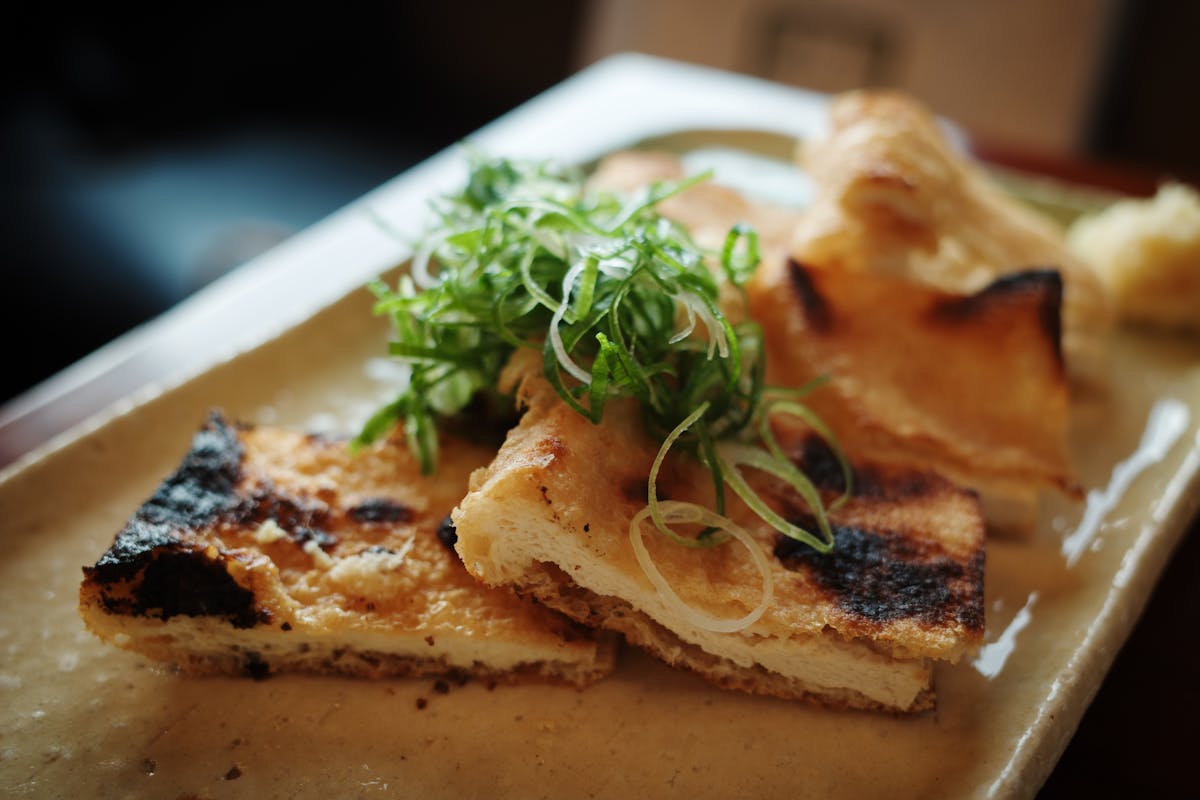Grilled tofu topped with fresh scallions on a ceramic plate