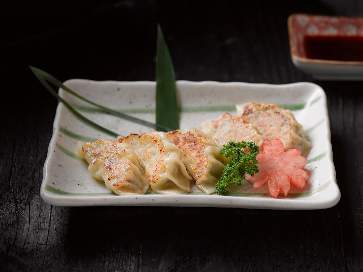 Golden pan-fried Japanese gyoza dumplings arranged on a ceramic plate with green garnish