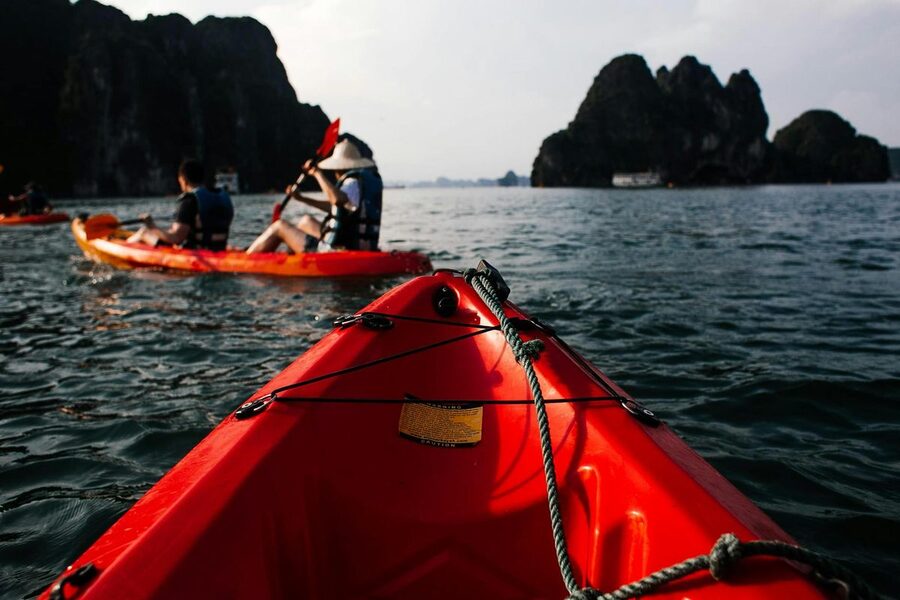 Orange kayak paddling through emerald waters near limestone cliffs