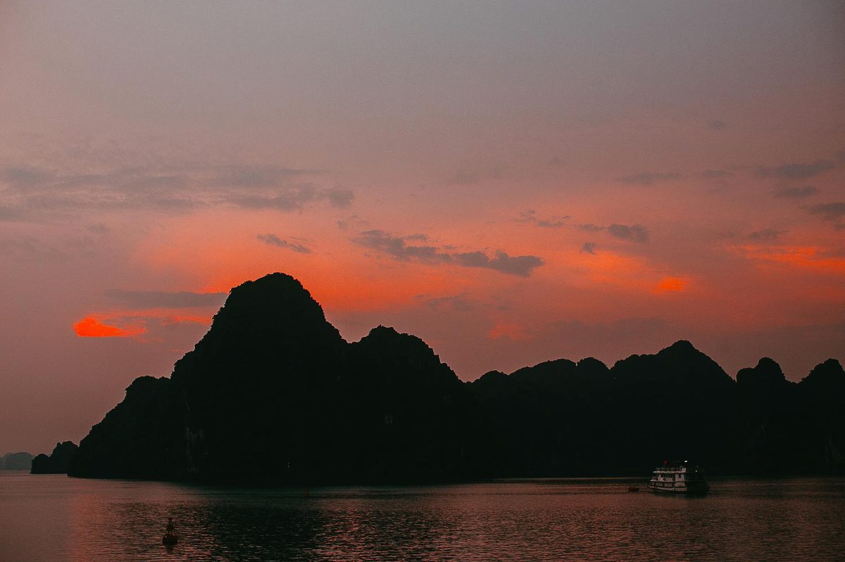 Twilight scene over Halong Bay with boat and mountain silhouettes