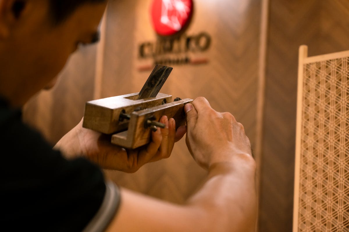 Close-up of a craftsman using a traditional Japanese hand plane on wood in a workshop setting
