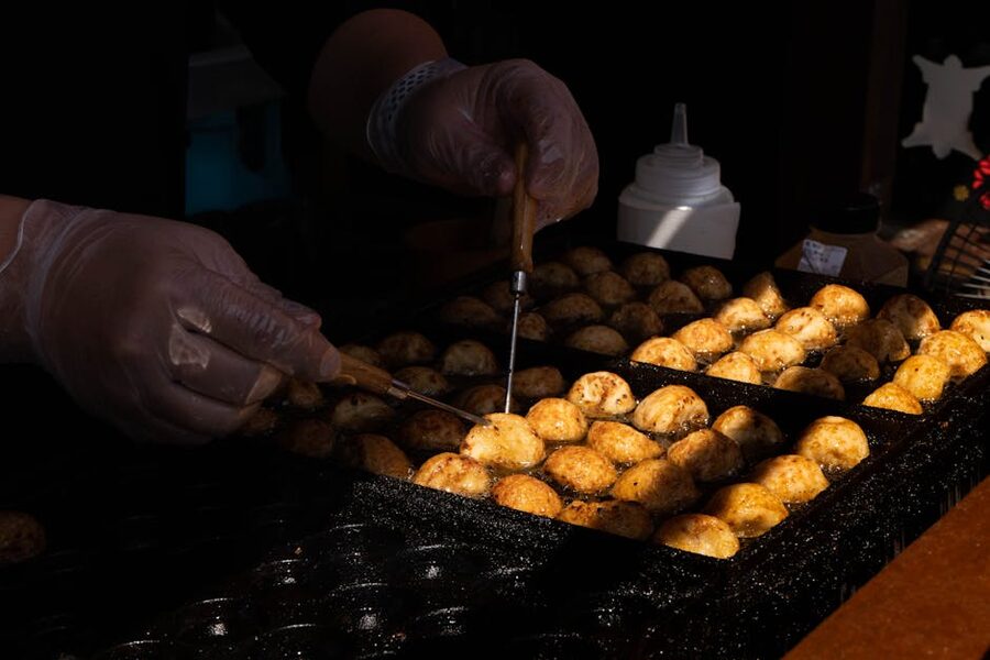 Hands turning takoyaki balls on a griddle