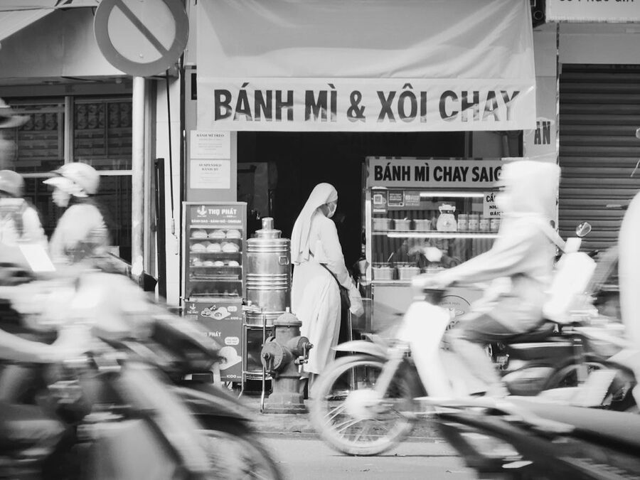 Banh mi vendor on a Ho Chi Minh City street with motorbikes passing by