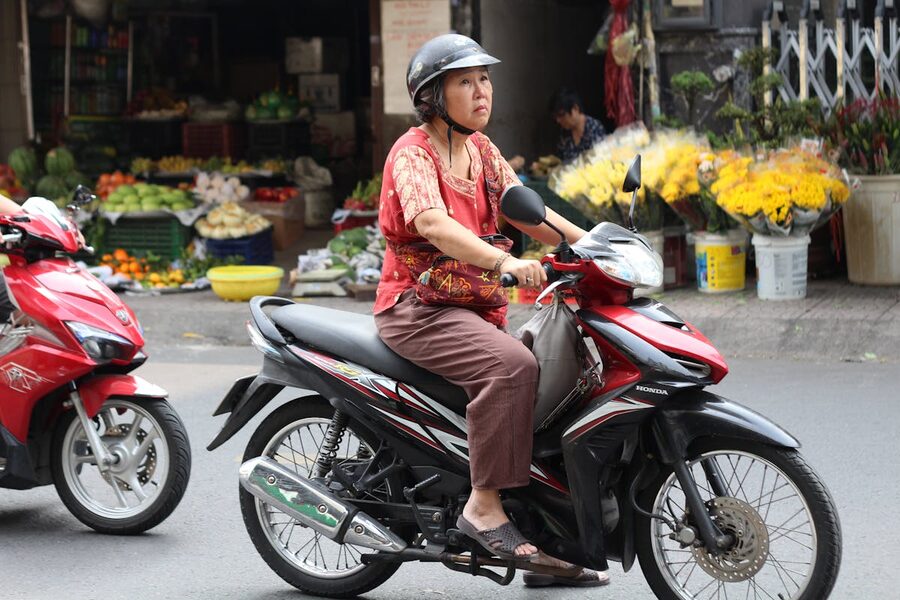 Woman riding a motorcycle past a market in Saigon