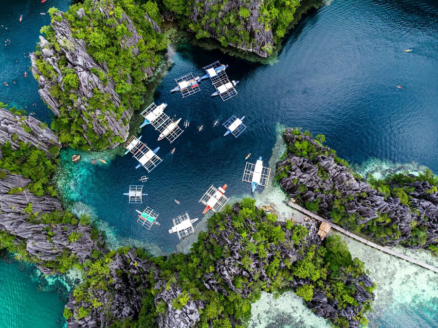 Aerial view of turquoise Big Lagoon with boats and limestone cliffs in El Nido Palawan
