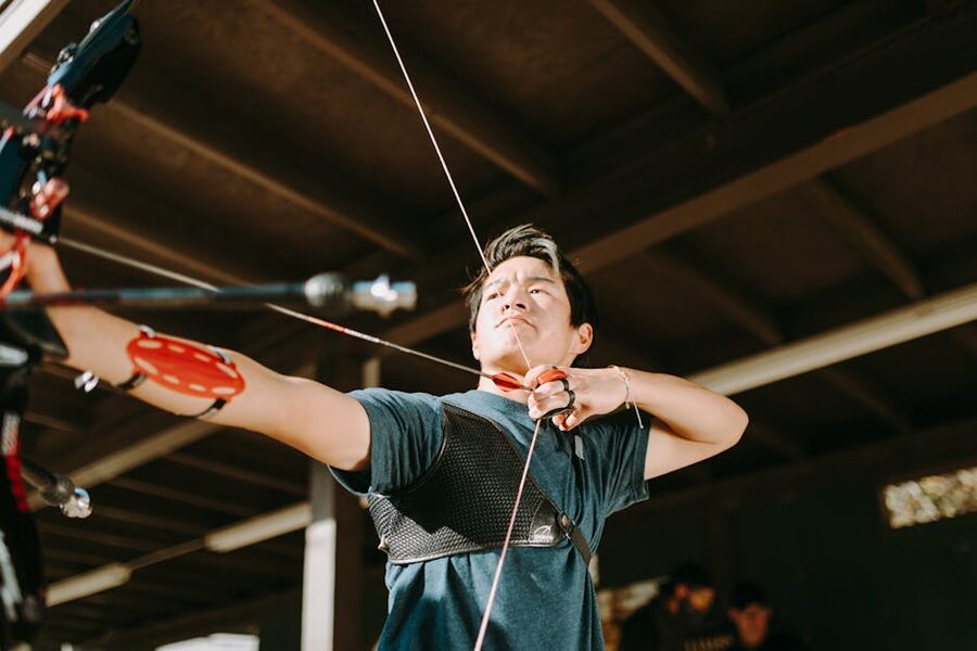 Focused young archer at indoor range drawing bow