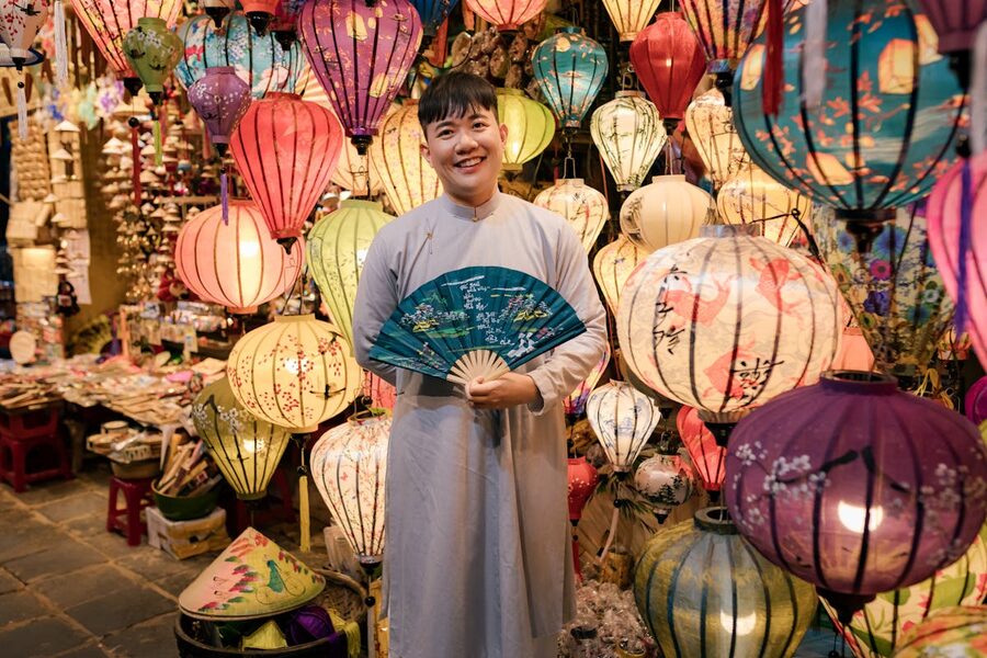 Smiling lantern vendor surrounded by colorful lanterns at a Hoi An market stall