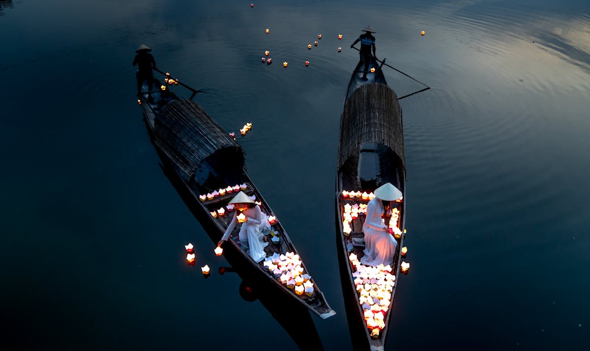 Women on wooden boats releasing paper lanterns on the Thu Bon River in Hoi An