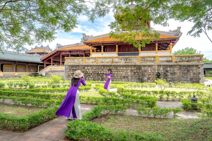 Women wearing traditional ao dai dresses walking through a temple garden at Hue Imperial City