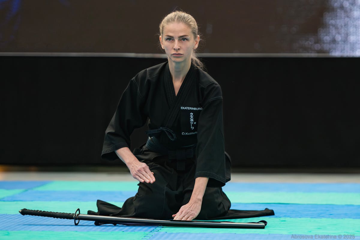 Martial artist in black gi performing iaido sword drawing technique indoors