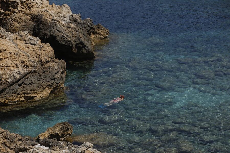 Woman snorkeling near rocky shore in clear water of Ibiza