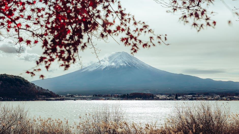 Mount Fuji viewed through red and orange autumn leaves with lake reflection