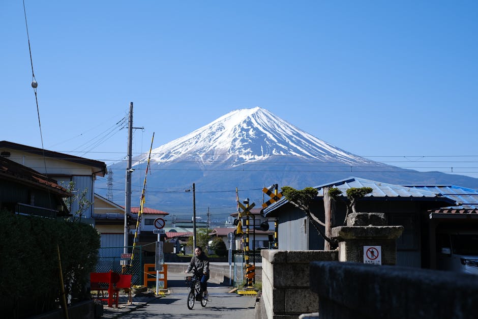 Person cycling near a railway crossing with Mount Fuji visible in the distance