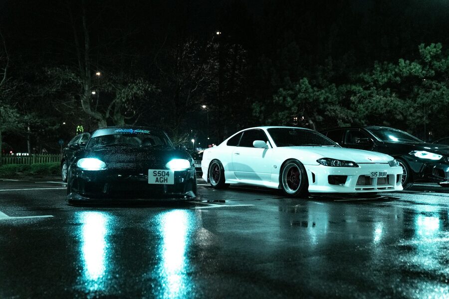 Two Japanese sports cars in a wet parking lot at night with moody lighting