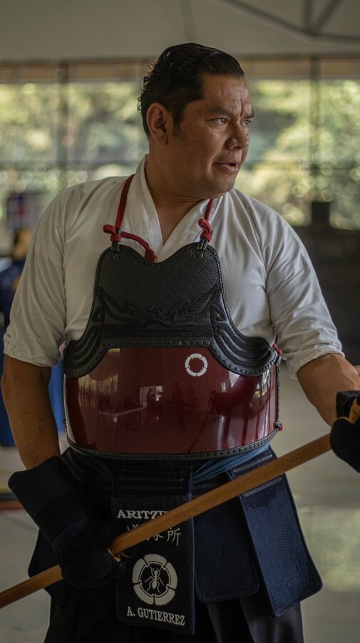 Person practicing kendo in a dojo wearing traditional armor and holding a shinai