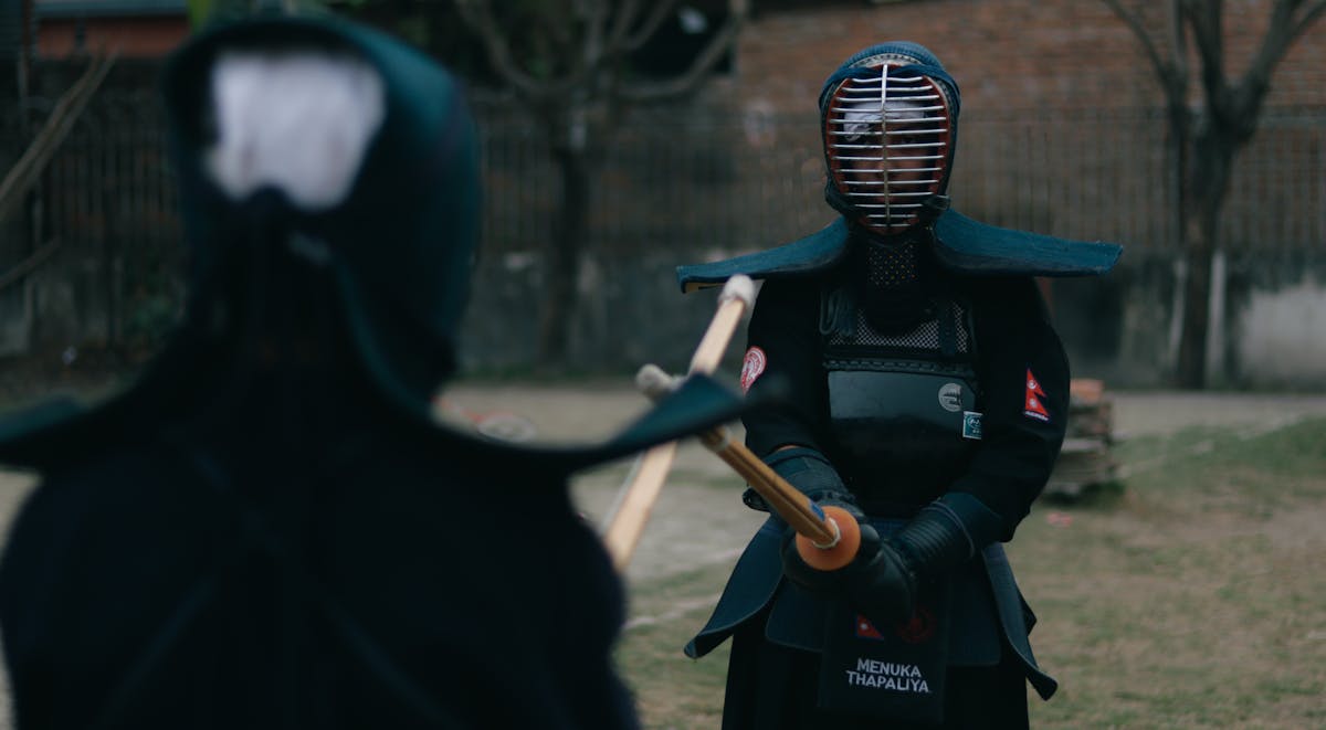 Two kendo practitioners in full armor sparring outdoors with bamboo swords