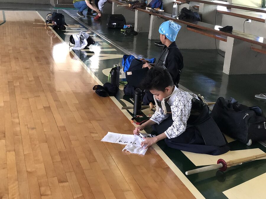 Kids in kendo gi and hakama preparing tenugui head cloths before practice