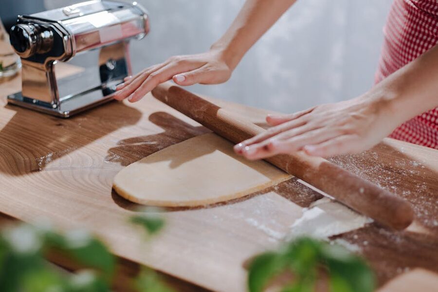 Kneading pasta dough on a wooden board with hands covered in flour