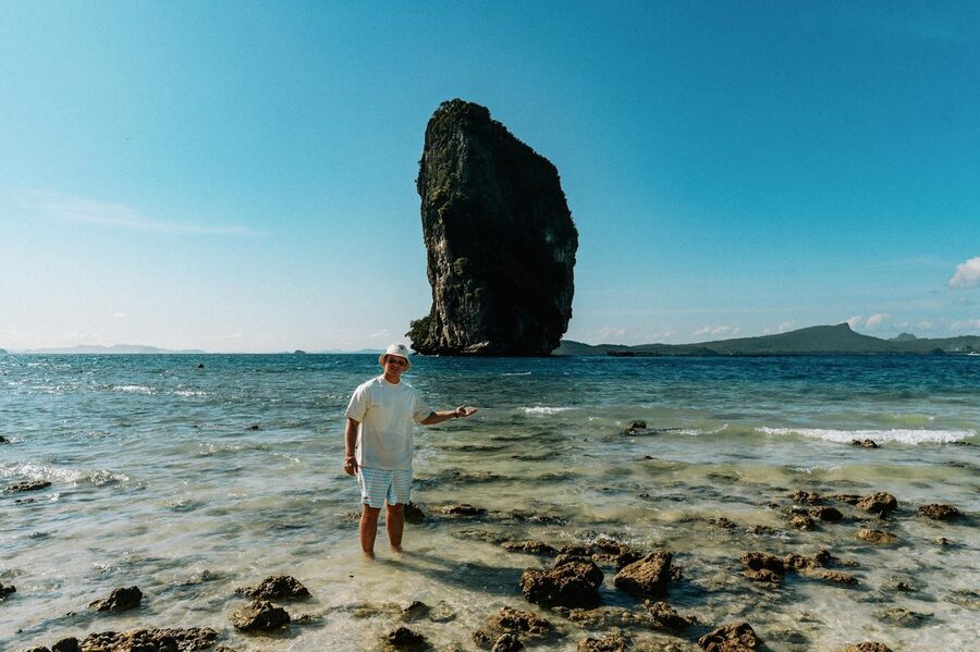 Person standing in shallow water near a limestone island under blue sky