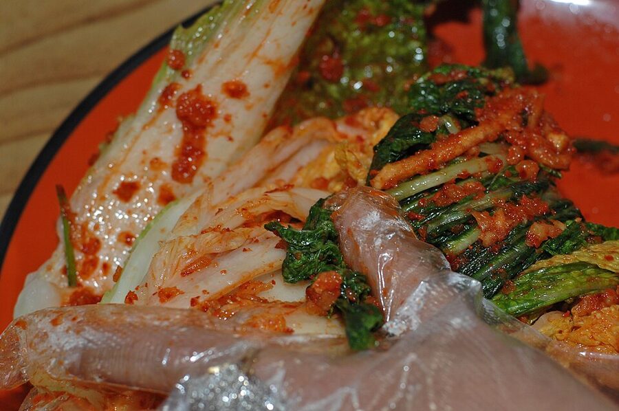 Hands mixing gochugaru paste into salted cabbage at a Korean kimchi class