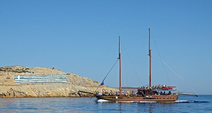 Pserimos beach with cruise boat anchored offshore Greek flag flying