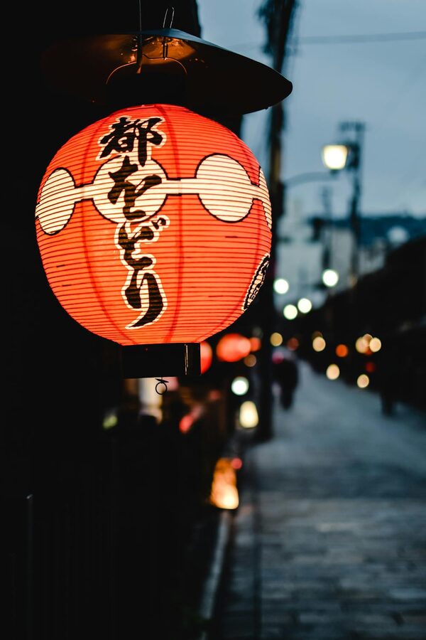 Single traditional lantern glowing warmly in a dark Kyoto alley at night