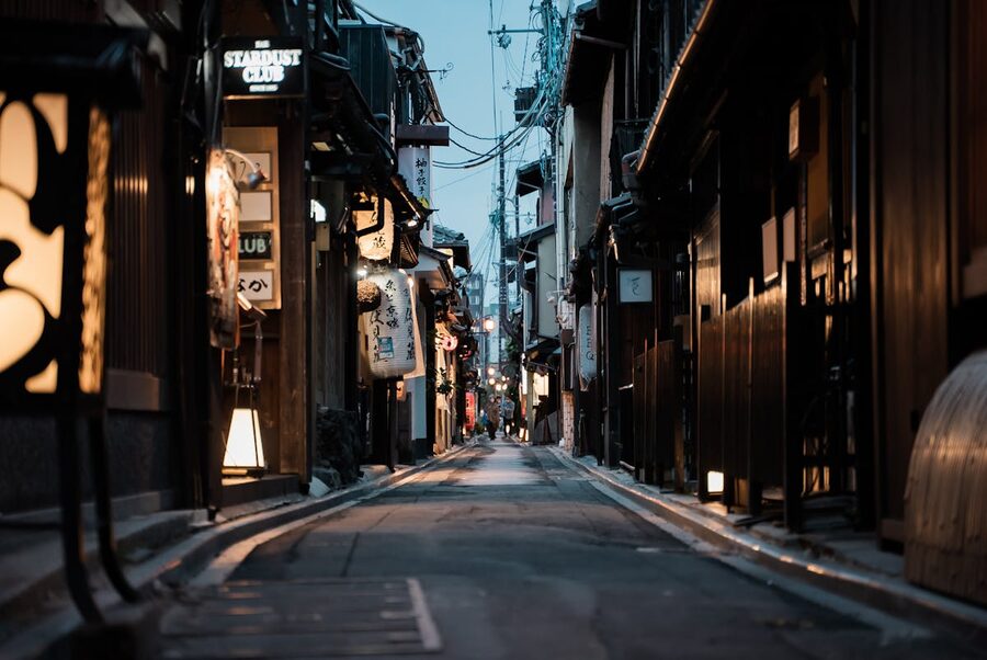 A narrow Kyoto street lined with traditional red lanterns and historic wooden buildings at dusk