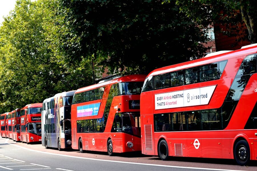 Row of red London double-decker buses parked near trees