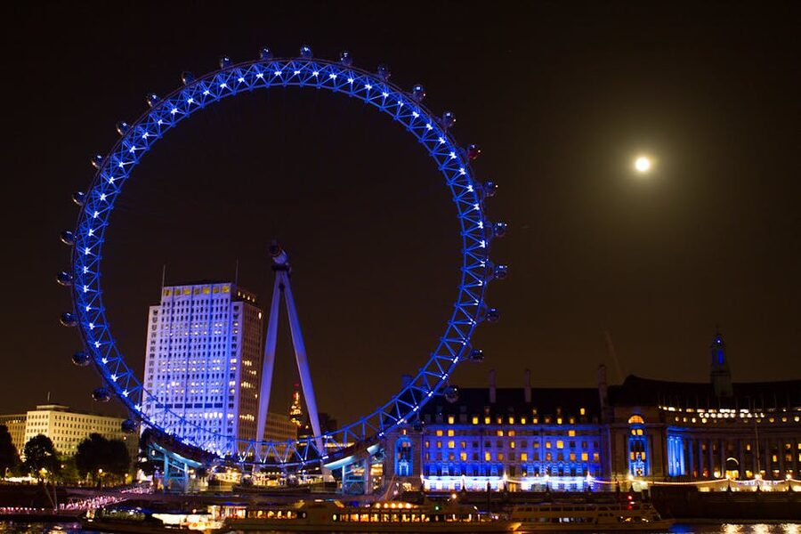 London Eye lit blue with full moon over the Thames at night