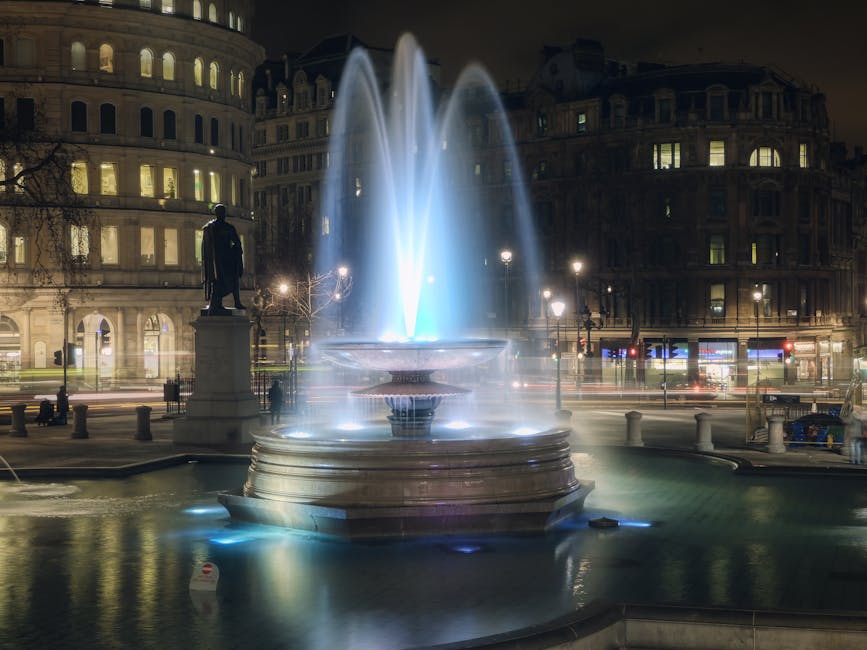 Trafalgar Square fountains lit blue and white at night with Nelson's Column
