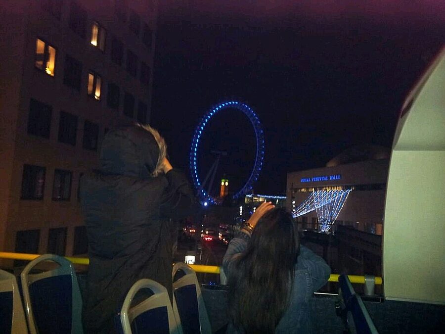 Big Ben framed through the London Eye at night from an open-top bus