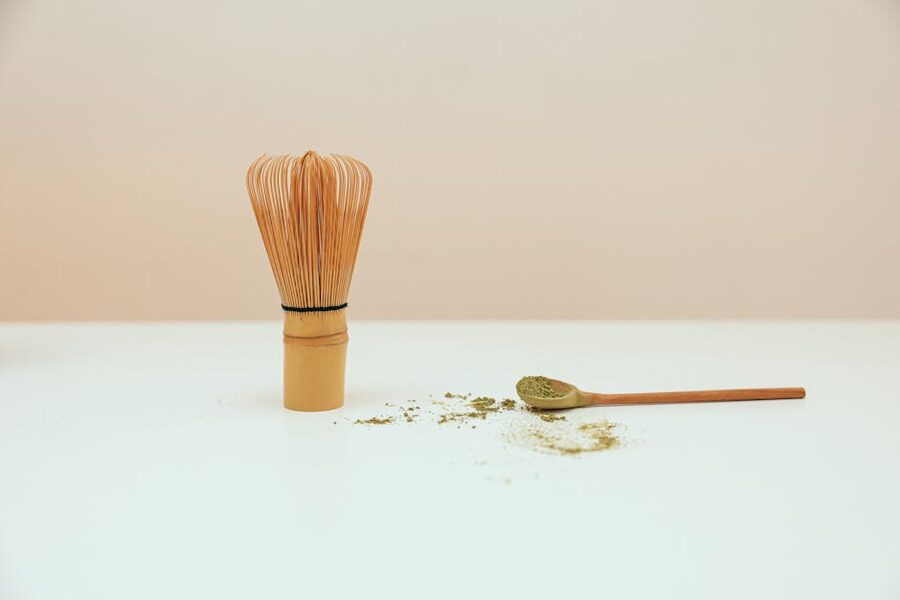 Bamboo whisk and matcha powder on wooden surface