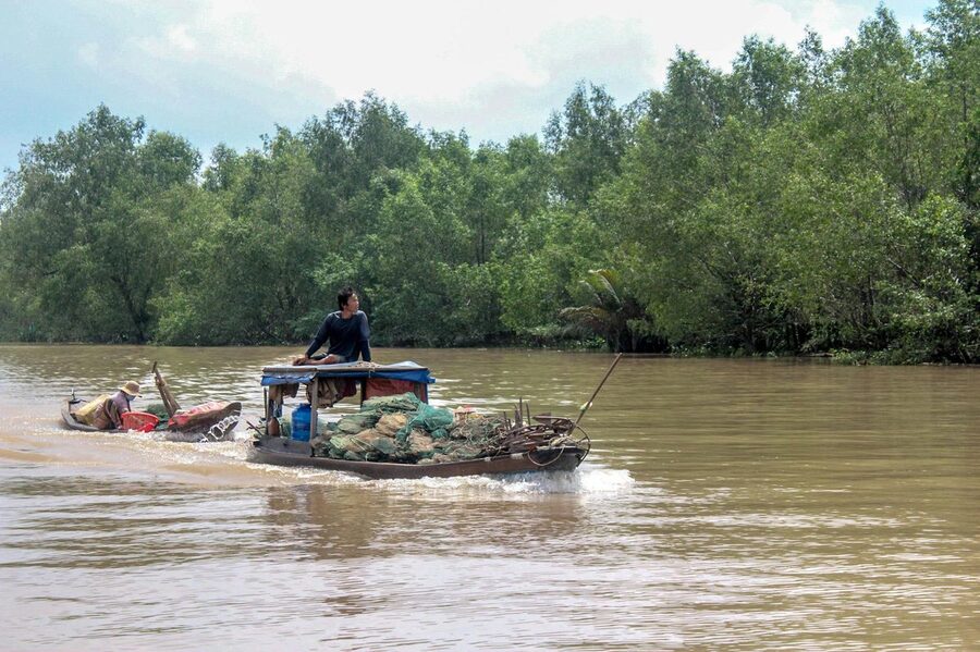 Man navigating a wooden boat on the Mekong River surrounded by greenery