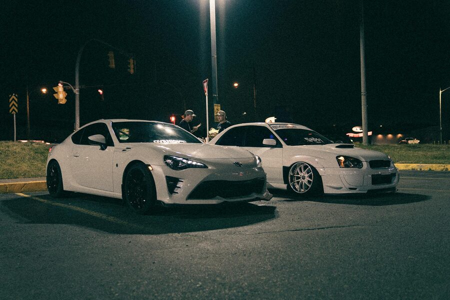 Two modified sports cars parked under streetlights at a nighttime car meet