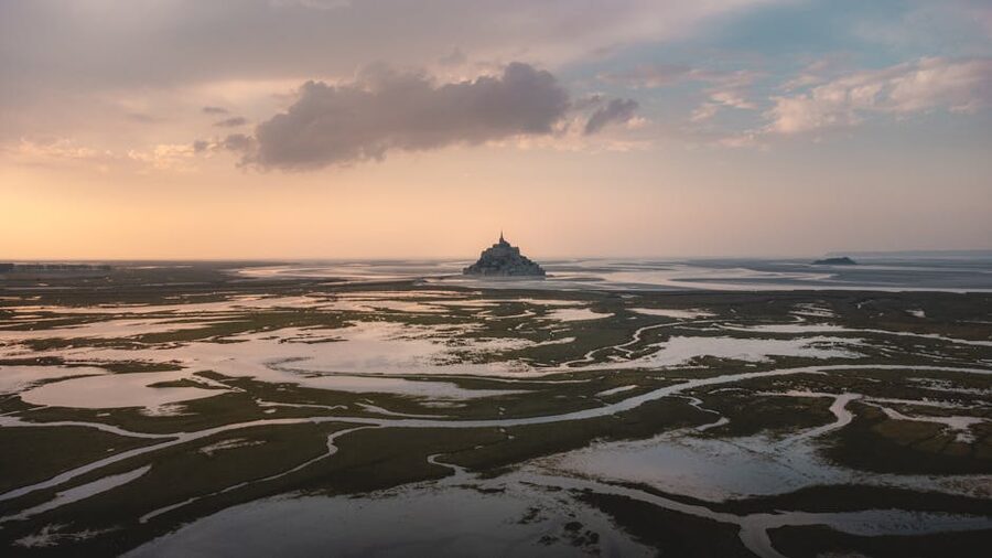 Aerial view of Mont Saint Michel during low tide at sunset with reflective marshlands