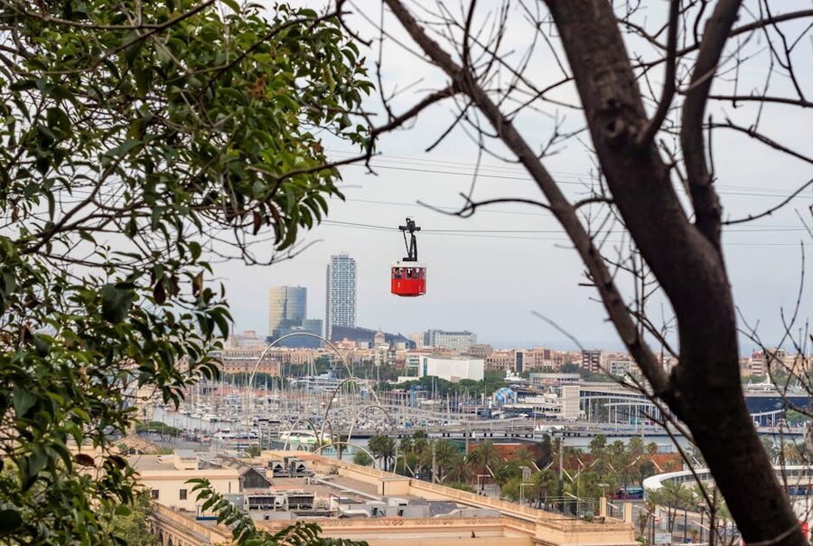 Red and white Montjuic cable car between trees with Barcelona skyline