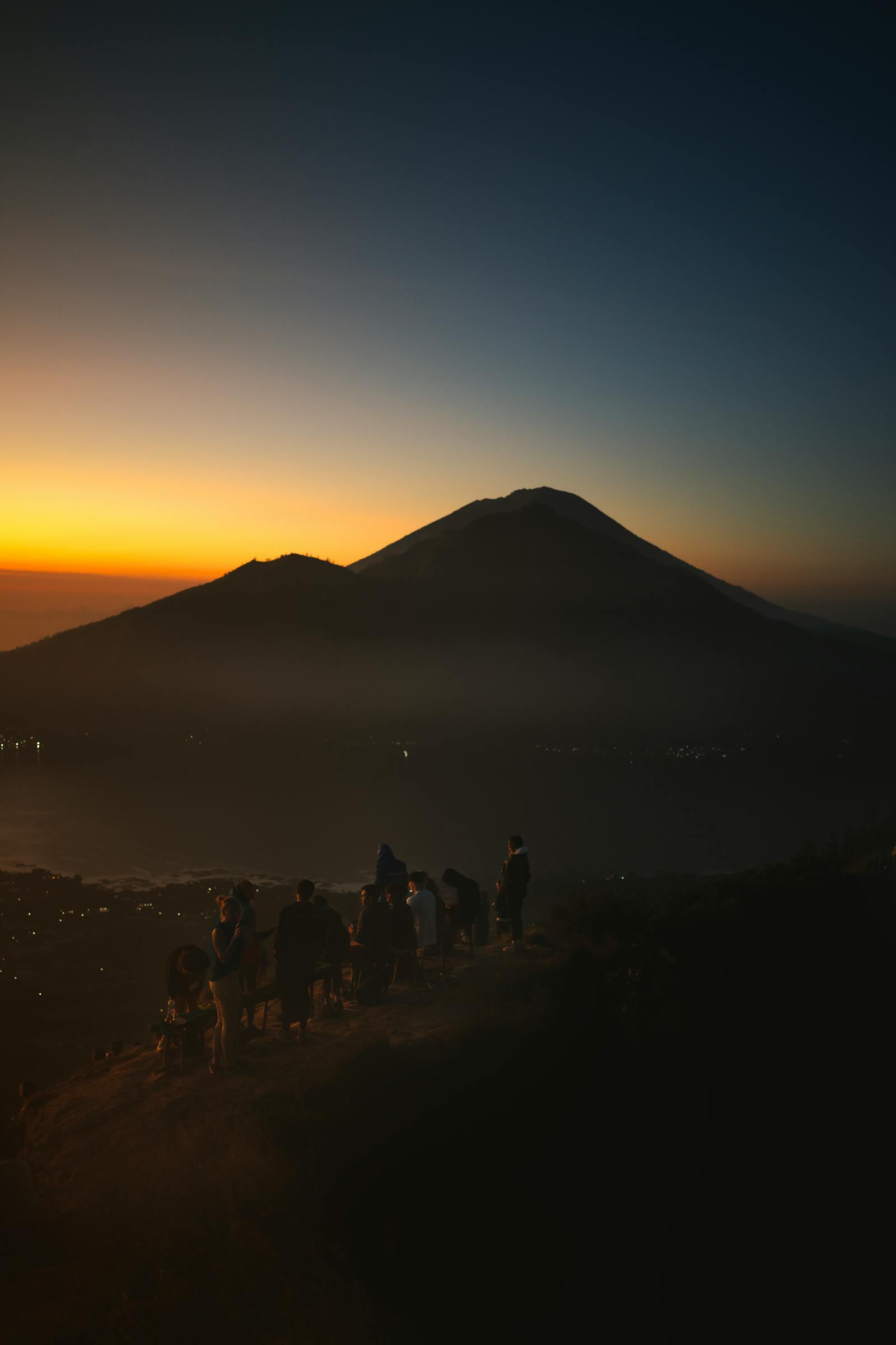 Silhouetted hikers on the volcanic ridge of Mount Batur against a pink and orange dawn sky