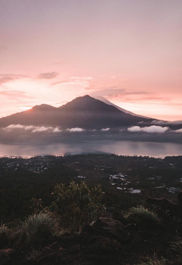 Dawn light breaking over a rocky trail on Mount Batur with the caldera visible below