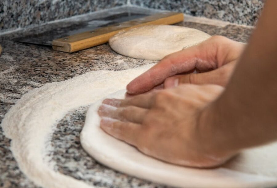 Hands kneading pizza dough on a floured surface