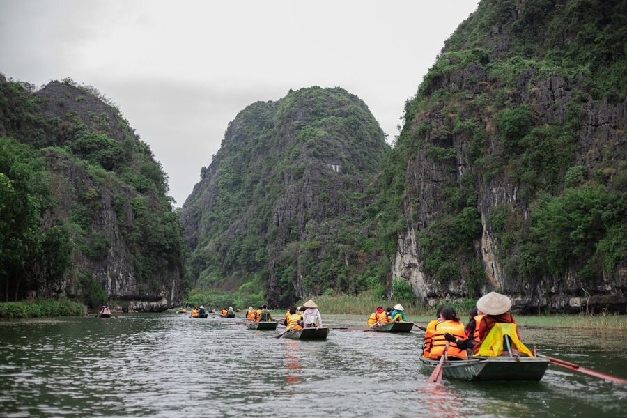 Tourists in boats floating through a narrow river canyon with limestone cliffs in Tam Coc