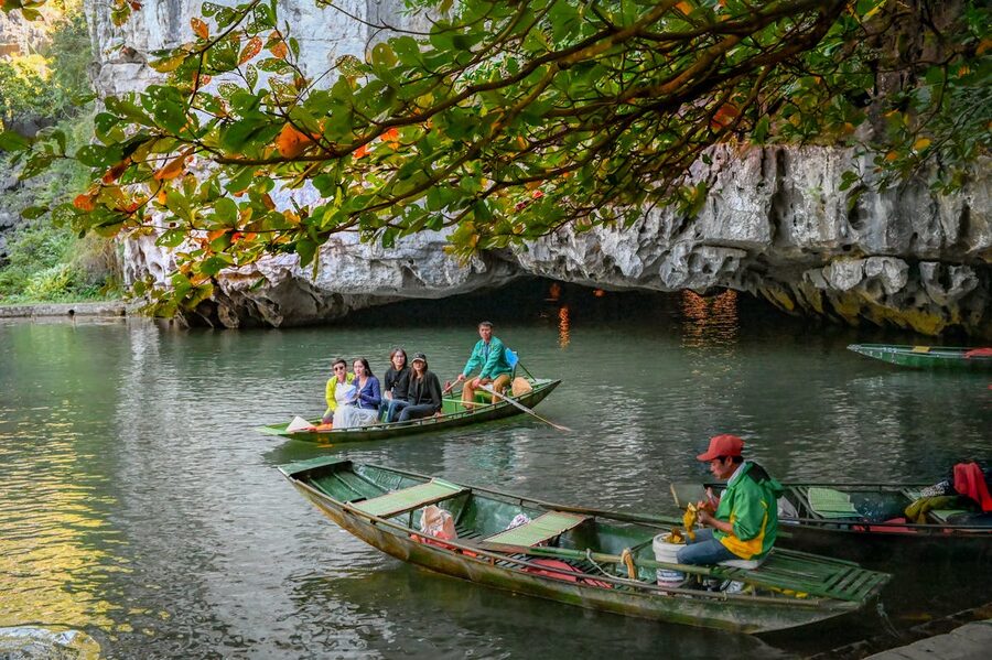 Tourists enjoying a scenic boat ride through Trang An Grottoes surrounded by lush karst landscape