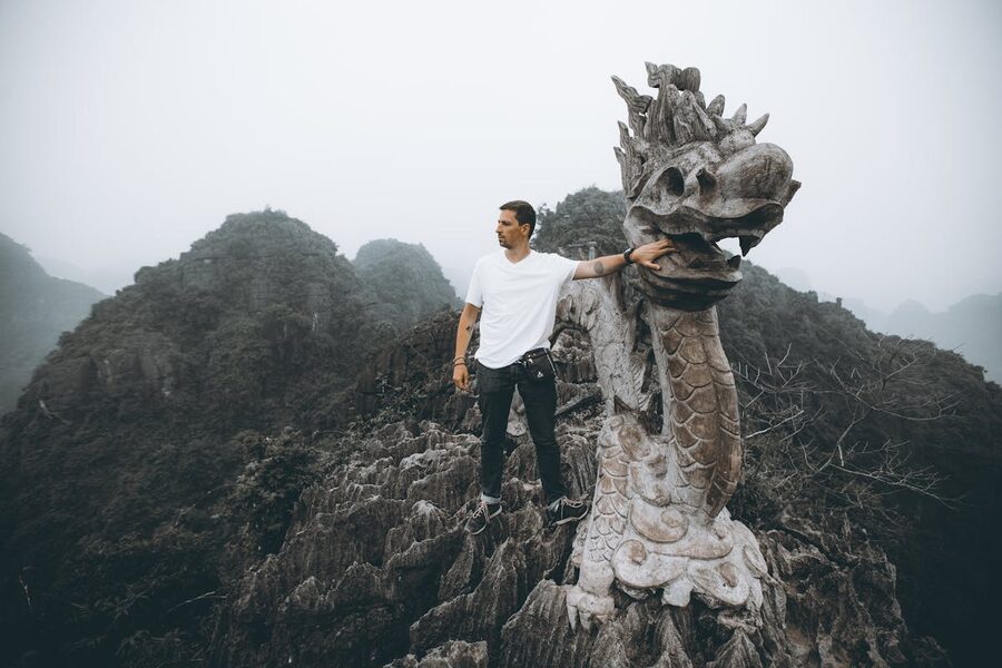 Man poses with a dragon sculpture atop Mua Cave amidst limestone peaks in Ninh Binh