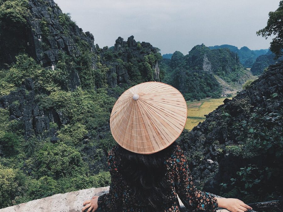 Woman in traditional Vietnamese conical hat overlooks stunning limestone cliffs in Ninh Binh